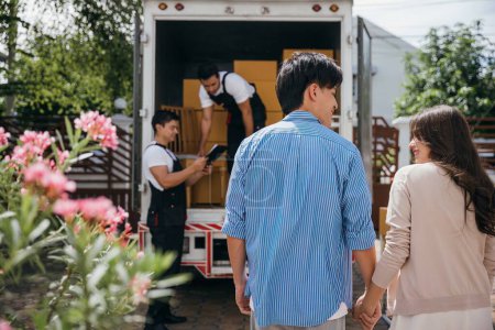 Photo for Assisted by a professional delivery team a couple transitions to their new home. Together they unload and lift cardboard boxes ensuring an organized and efficient move. Moving Day Concept - Royalty Free Image