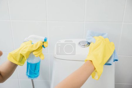 Téléchargez les photos : La femme de ménage en gants jaunes nettoie méticuleusement le siège des toilettes à l'aide d'un chiffon. Son accent sur la pureté et l'hygiène incarne le dévouement de la gouvernante aux soins de la salle de bain. Concept de soins de santé ménagère - en image libre de droit