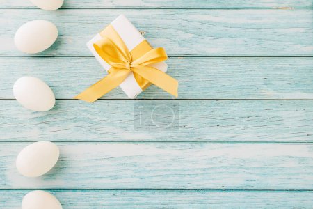 Téléchargez les photos : Joyeuse fête de Pâques. Dessin d'arrière-plan de bannière de vacances avec oeufs de Pâques blancs et boîte cadeau sur fond bleu en bois avec espace de copie, carte de vœux de célébration - en image libre de droit