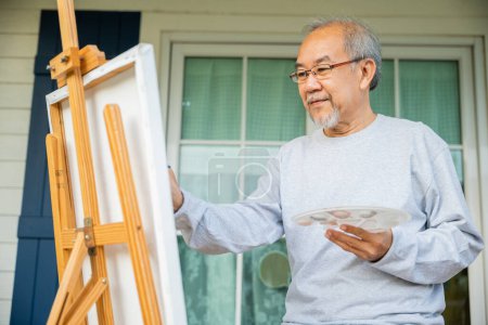 Téléchargez les photos : Artiste. Vieil homme asiatique peinture tableau en utilisant le pinceau et la couleur à l'huile sur toile, style de vie personnes âgées sourire peinture à son chevalet, Bonne retraite et concept d'activité - en image libre de droit