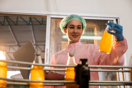 Téléchargez les photos : Managerial femme inspecte les bouteilles sur les machines à l'aide d'un ordinateur portable dans l'usine. Le contrôle de la qualité et le contrôle des liquides garantissent des normes industrielles élevées. Le contrôle axé sur la technologie est la clé. - en image libre de droit