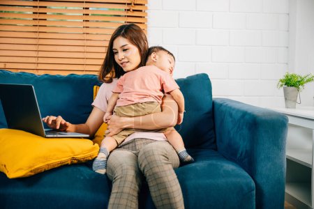 Photo for Balancing business and family a mother types on her laptop as her baby daughter naps on the sofa. The affectionate care and responsibility are beautifully captured in this portrait. - Royalty Free Image