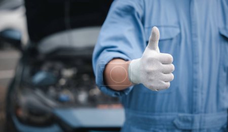 Photo for Mechanic in jumpsuit checks car gives thumbs up. Expertise in repair and service ensuring safety and quality. Skilled technician working in automotive industry smiling. - Royalty Free Image