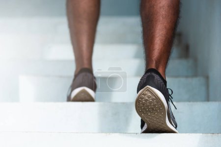 Téléchargez les photos : Gros plan chaussures d'athlète de jambes jeune coureur de sport homme noir étape en cours d'exécution jusqu'à monter des escaliers faire de l'entraînement cardio sport séance d'entraînement à la rue en plein air, exercice sain avant concept d'entraînement - en image libre de droit