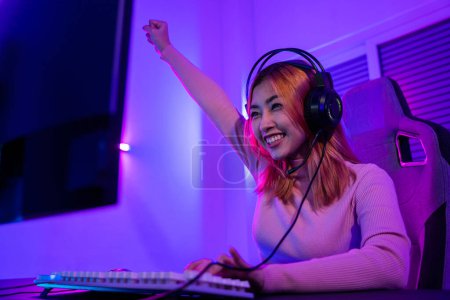 Photo for Winning. Young woman in gaming headphones playing video game online at home neon room feel excited, Happy Gamer young plays online video games computer she raises hands to wins tournament, E-Sport - Royalty Free Image