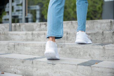 Photo for Close-up of a womans legs in sneakers ascending the city stairway. Every step she takes signifies determination and progress on her journey to success and achievement. step up - Royalty Free Image