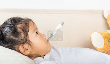 Téléchargez les photos : Enfant malade. Mère vérifiant la température de sa fille malade avec thermomètre dans la bouche, enfant couché au lit prenant la mesure de sa température pour la fièvre et la maladie - en image libre de droit