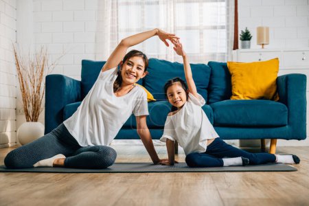 Téléchargez les photos : Dans leur maison, une mère asiatique devient professeur de yoga pour sa fille, promouvant l'harmonie de la force et l'éducation. Les sourires et la concentration sont évidents dans ce moment heureux de familles. - en image libre de droit