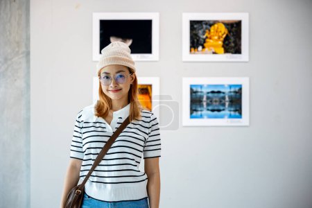 Foto de Visitante mujer sonriendo en la colección de galería de arte en frente cuadros enmarcados imágenes en la pared blanca, estilo de vida Asiática ver en el marco de la foto a apoyarse en la exposición exposición galería de obras de arte - Imagen libre de derechos