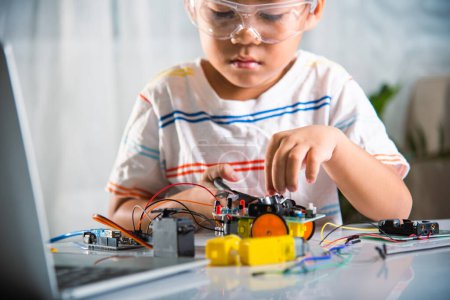 Foto de Pequeño niño apriete la tuerca con un destornillador para ensamblar el juguete del coche, niño asiático montando el proyecto de tarea de coche robot Arduino en casa, lección de aprendizaje escolar de taller de tecnología de IA de educación - Imagen libre de derechos
