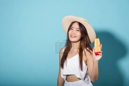 Photo for Beautiful Asian young woman holding body lotion on hand in studio shot isolated on blue background, Brunette female hold cream sunblock bottle, tube of sunscreen, Beauty cosmetics facial treatment - Royalty Free Image