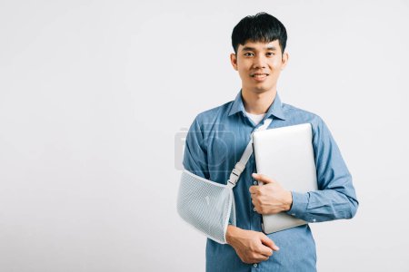 Téléchargez les photos : Despite a broken arm, a dedicated business man works with a laptop, supported by a splint. Studio shot isolated on white, highlighting resilience and recovery. Copy space is featured. - en image libre de droit