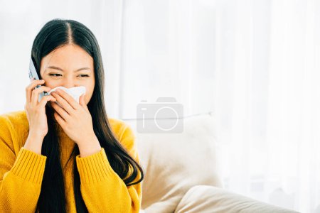 A sick female seeks care calling doctor wiping nose sneezing on sofa. An ill young girl discusses influenza symptoms with practitioner on phone seeking medicine. Portraying patient care at home.