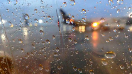 Téléchargez les photos : Terrain de l'avion pluvieux à travers la fenêtre de l'avion, fond de voyage abstrait, au revoir photo conceptuelle - en image libre de droit