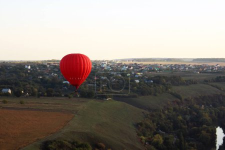 Téléchargez les photos : Ballon à air chaud (aérostat) au-dessus des champs verts et d'une ville derrière - en image libre de droit