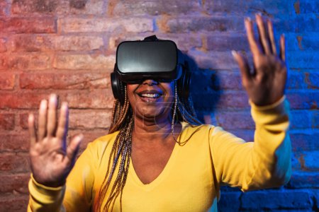Foto de Mujer africana mayor divirtiéndose con gafas de realidad virtual futurista - Concepto de entretenimiento de juegos de tecnología - Imagen libre de derechos