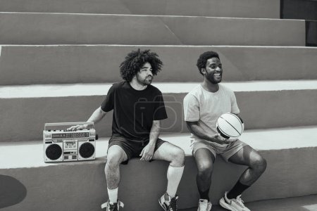 Foto de Hombres afroamericanos felices escuchando música dentro de la cancha de baloncesto con equipo de música vintage - Estilo de vida urbano de la gente de la calle - Edición en blanco y negro - Imagen libre de derechos