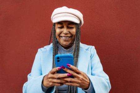 Foto de Mujer africana mayor que se divierte utilizando el teléfono inteligente móvil al aire libre - Imagen libre de derechos