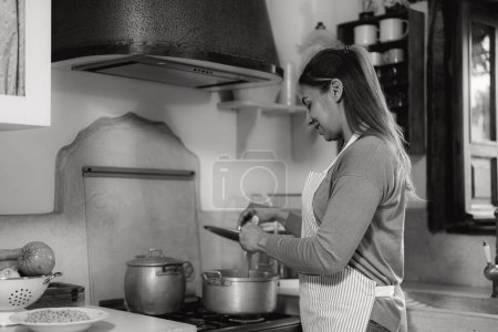 Téléchargez les photos : Femme latine préparant la recette de nourriture dans sa maison - Montage noir et blanc - en image libre de droit