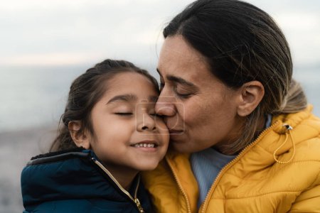Téléchargez les photos : Bonne mère latine ayant un moment tendre avec son enfant pendant les vacances d'hiver - concept de famille et d'amour - en image libre de droit