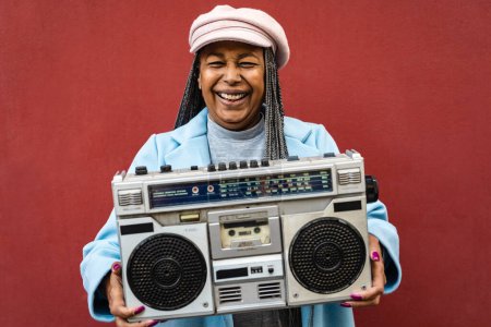 Foto de Happy trendy senior African woman having fun listening to music with vintage boombox stereo - Imagen libre de derechos