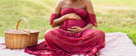 Foto de Mujer africana acariciando su vientre embarazada mientras hace un picnic en el parque - Concepto de estilo de vida de maternidad - Imagen libre de derechos