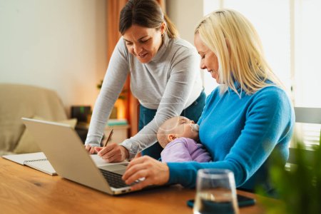 Photo for Happy lesbian couple working on laptop while their small baby is sleeping - LGBT family and technology concept - Royalty Free Image