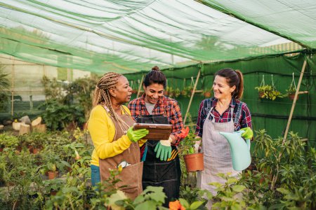 Foto de Feliz multirracial mujeres trabajando juntos en plantas y flores jardín tienda - Imagen libre de derechos