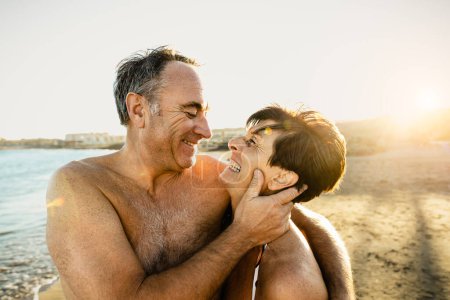 Téléchargez les photos : Heureux couple de personnes âgées ayant un moment romantique sur la plage au coucher du soleil pendant les vacances d'été concept de relation avec les personnes âgées - en image libre de droit