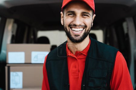 Photo for Young courier delivery man smiling into the camera while standing in front of his van transportation - Royalty Free Image