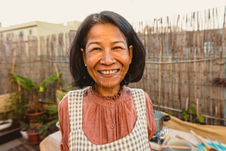 Téléchargez les photos : Heureuse femme thaïlandaise avoir du plaisir à sourire devant la caméra tout en préparant la recette de nourriture à la maison patio - en image libre de droit