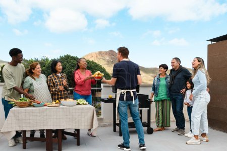 Téléchargez les photos : Des amis multigénérationnels s'amusent à faire un barbecue sur le toit de la maison - Heureux gens multiraciaux cuisiner ensemble - en image libre de droit