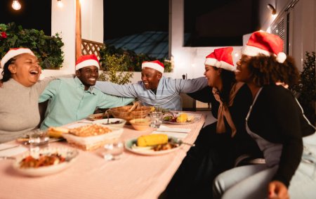 Foto de Felices familias africanas celebran las fiestas navideñas cenando juntas en casa - Imagen libre de derechos