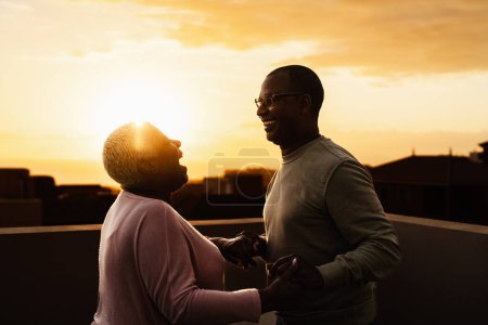 Téléchargez les photos : Heureux couple de personnes âgées latines ayant moment romantique sur le toit pendant l'heure du coucher du soleil - Les personnes âgées aiment concept - en image libre de droit