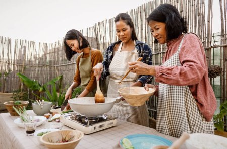Foto de Sudeste asiático madre con su hijas tener divertido preparación tailandés comida receta juntos en casa patio - Imagen libre de derechos