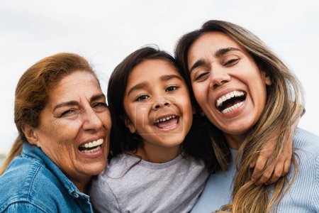 Foto de Feliz familia hispana multigeneracional sonriendo a la cámara - Niño divirtiéndose con su madre y su abuela al aire libre - Imagen libre de derechos