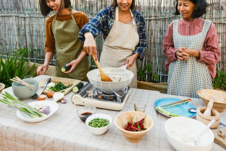 Foto de Sudeste asiático madre con su hijas tener divertido cocinar tailandés comida receta juntos en casa patio - Imagen libre de derechos