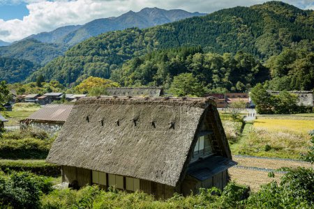Foto de Pueblo japonés de Shirakawago durante octubre en otoño temporada de follaje otoño. Shirakawa casa tradicional en el techo del triángulo con un fondo de campo de arroz, montaña de pino y cielo nuboso claro después. - Imagen libre de derechos
