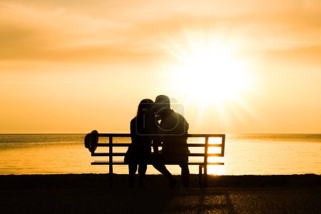 Foto de Feliz pareja en un banco junto al mar en la naturaleza en la silueta de viaje - Imagen libre de derechos