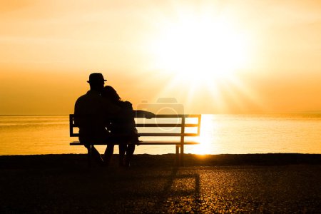 Foto de Feliz pareja en un banco junto al mar en la naturaleza en la silueta de viaje - Imagen libre de derechos