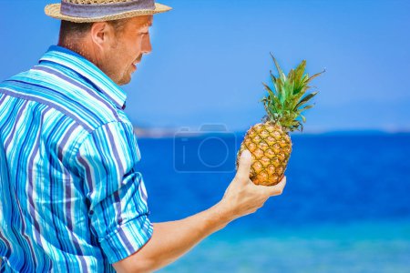 Téléchargez les photos : Ananas dans les mains d'un homme au bord de la mer dans la nature sur un fond de voyage - en image libre de droit