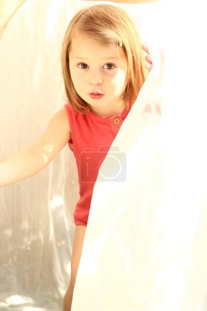 Téléchargez les photos : Petite fille regardant dehors avec rideau - en image libre de droit