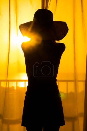 Photo for A Silhouette of a girl on a loggia balcony background. A happy woman with a hat in her hands while on vacation traveling. - Royalty Free Image