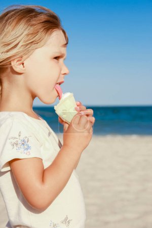 Téléchargez les photos : Enfant heureux sur la plage près de la piscine en plein air manger de la crème glacée dans le parc d'été - en image libre de droit