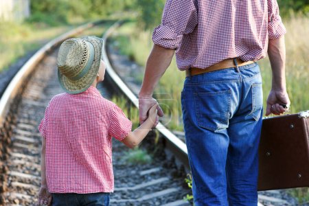 Téléchargez les photos : Mains de parent et fils en chapeau de cow-boy près de la voie ferrée avec valise - en image libre de droit