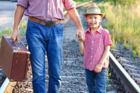 Foto de Manos de padre e hijo en sombrero de vaquero cerca del ferrocarril con maleta - Imagen libre de derechos