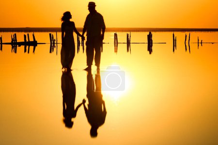 Téléchargez les photos : Couple heureux en mer avec reflet de l'eau silhouette fond - en image libre de droit