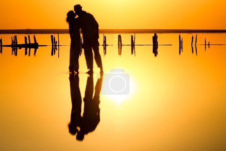 Téléchargez les photos : Couple heureux en mer avec reflet de l'eau silhouette fond - en image libre de droit
