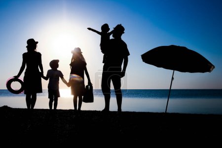 Téléchargez les photos : Bonne famille au bord de la mer au coucher du soleil en silhouette de voyage dans la nature - en image libre de droit