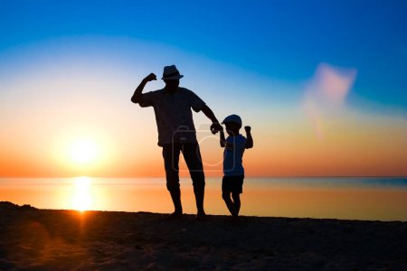 Foto de Padres felices con el niño junto al mar jugar en la silueta de la naturaleza de viaje - Imagen libre de derechos